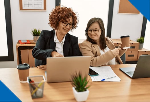 Una mujer en condición de discapacidad, revisando información en un portátil, junto a su asesora.
